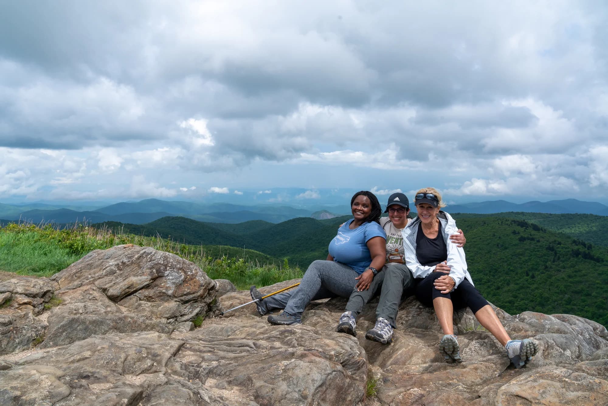 Three women seated on a rocky hilltop overlooking the Blue Ridge Mountains during a Skyterra retreat outing